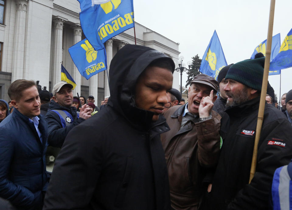 Zhan Beleniuk, world wrestling champion and lawmaker of President Volodymyr Zelenskiy's 'Servant of the People' party, center, passes through the crowd of angry protesters outside the parliament building after a parliament session in Kyiv, Ukraine, Wednesday, Nov. 13, 2019. After an hours-long debate in parliament in which tempers flared, the majority of Ukrainian lawmakers passed a bill lifting the ban on buying and selling farmland. It received 240 votes, requiring 226 to pass. (AP Photo/Efrem Lukatsky)