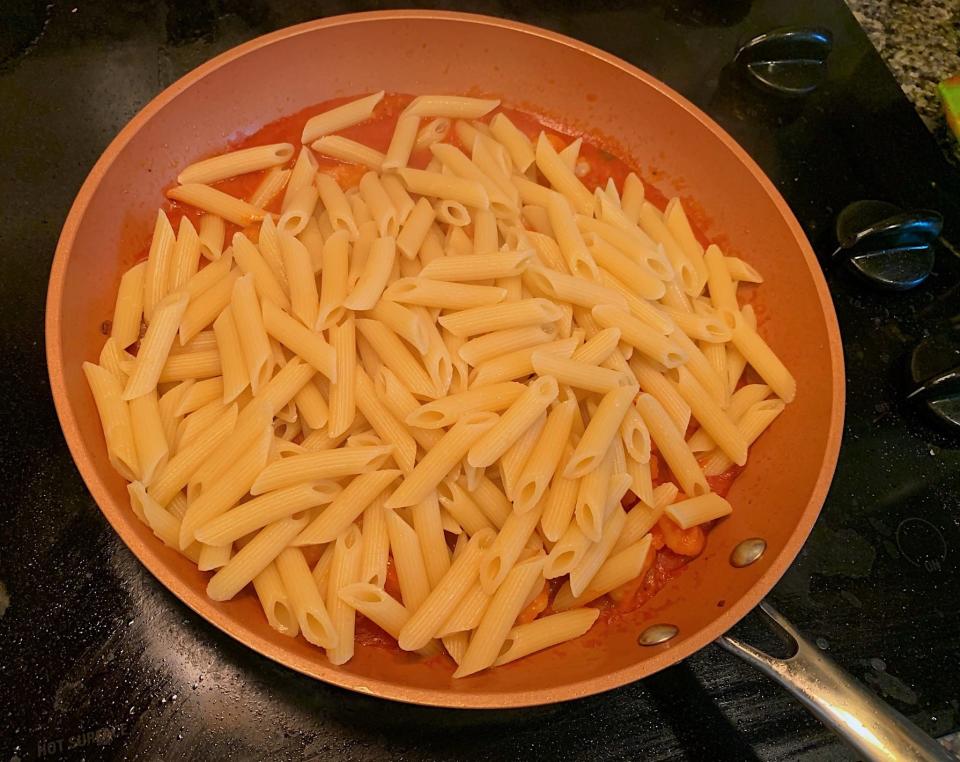 The penne pasta added to the pan with the sauce and shrimp