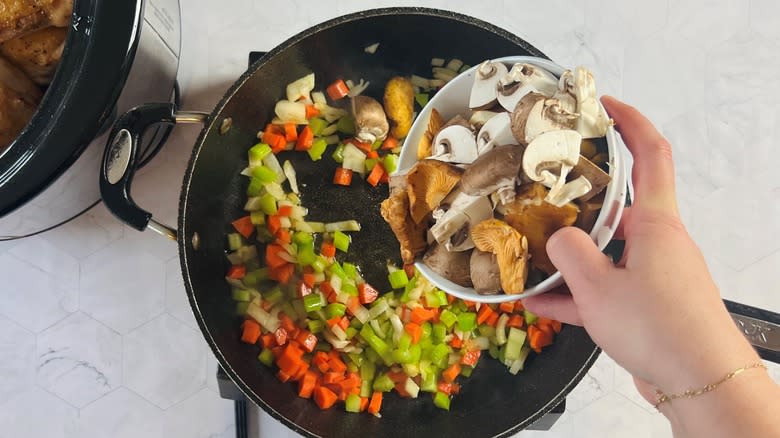 Mushrooms being added to a pan full of other vegetables