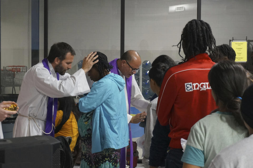 The Rev. Brian Strassburger, left, and Flavio Bravo, center, bless migrants during Mass at the Humanitarian Respite Center for migrants across the bus station in McAllen, Texas, on Dec. 15, 2022. Pregnant women are usually admitted far more quickly than others to the United States to pursue their asylum claims, but many more people are expected to cross the border if asylum policies change. (AP Photo/Giovanna Dell'Orto)