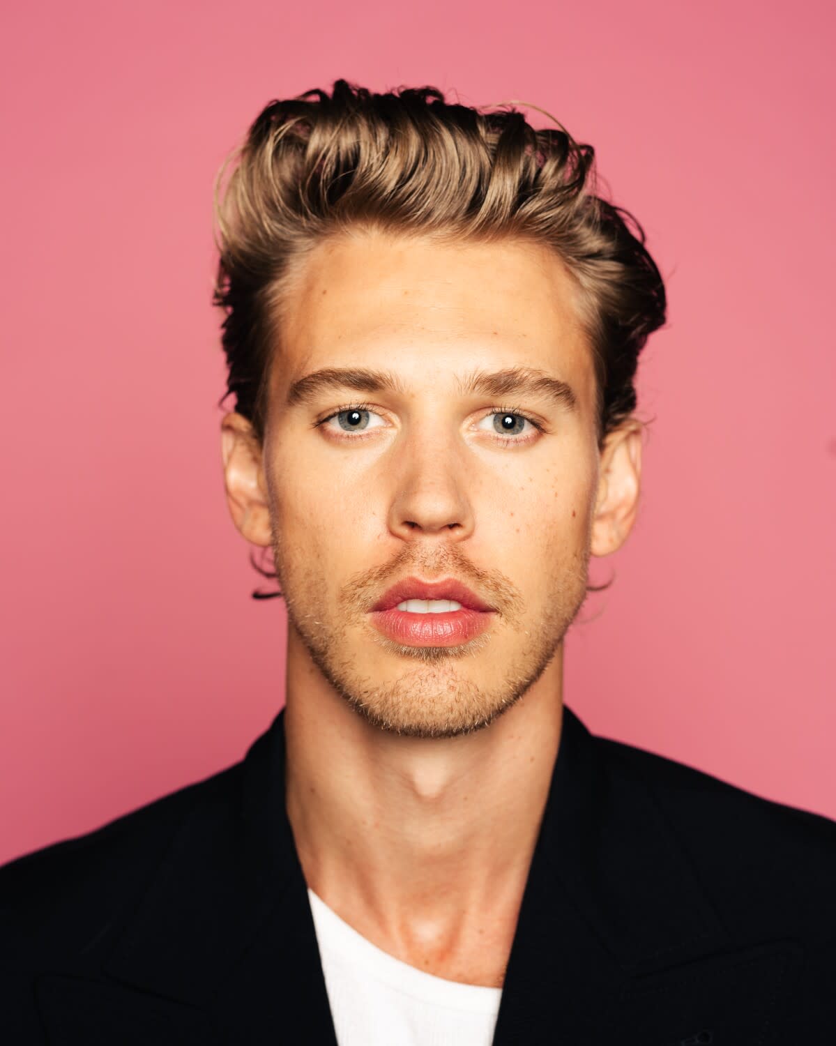 A man with blond hair poses for a portrait against a pink backdrop.