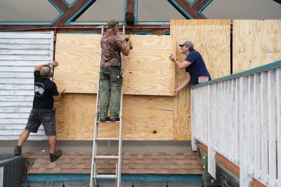 (from left) Chris Laite, Clay Brooks and Jordan Keeton, owner of the restaurant ’83 West’ board up the building before the storm on Aug. 29, 2023.