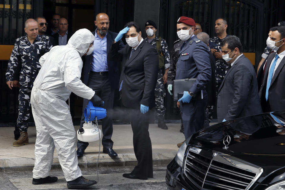 A paramedic sprays Lebanese Prime Minister Hassan Diab with disinfectant as he arrives for a parliament meeting, in Beirut, Lebanon, Tuesday, April 21, 2020. Lebanon's parliament began a three-day legislative session at a Beirut theater so that legislators can observe social distancing measures due to the coronavirus pandemic, as protests against the country's ruling elite in the crisis-hit country resumed. (AP Photo/Bilal Hussein)