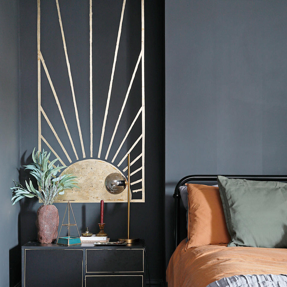 a black bedroom with metal framed bed and bedside table and a gold sunshine decal on the wall