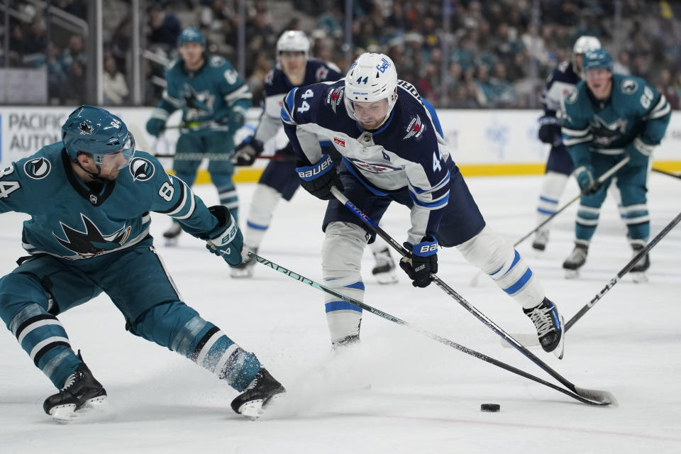 Winnipeg Jets defenseman Josh Morrissey (44) moves the puck while defended by San Jose Sharks defenseman Jan Rutta, left, during the second period of an NHL hockey game Tuesday, Dec. 12, 2023, in San Jose, Calif. (AP Photo/Godofredo A. Vásquez)