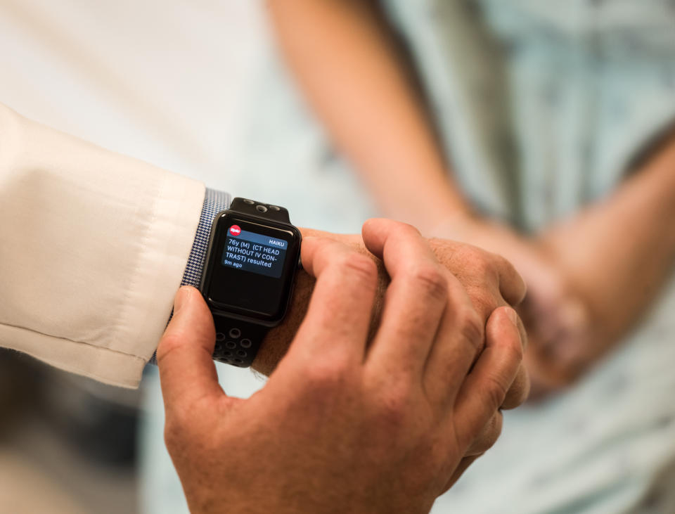 A person in a white lab coat looking at patient records on an Apple Watch