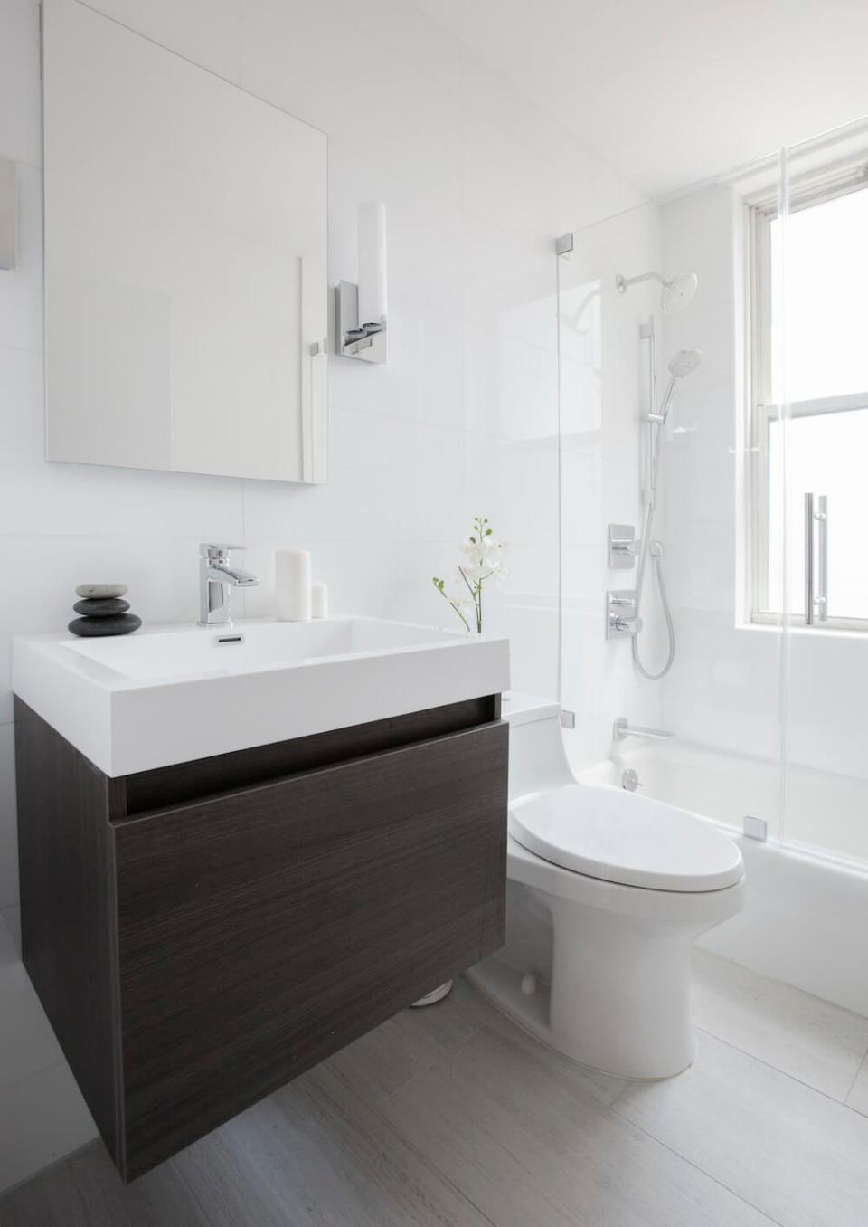 A small white bathroom with a wooden vanity under a white porcelain sink.