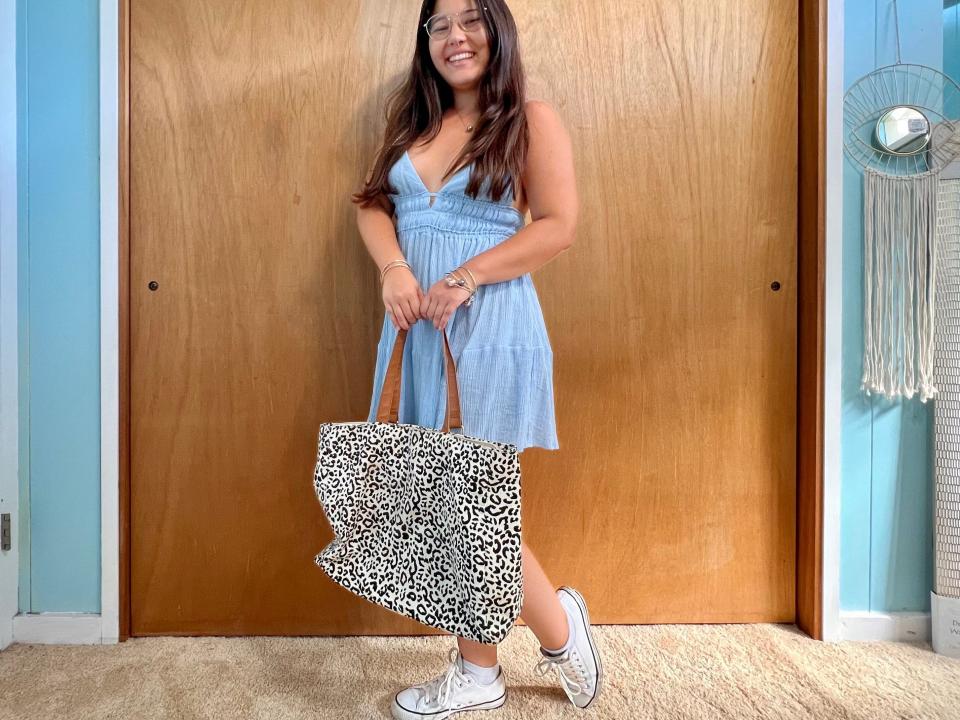 Author poses wearing baby-blue dress, white sneakers, and cheetah-print tote bag.