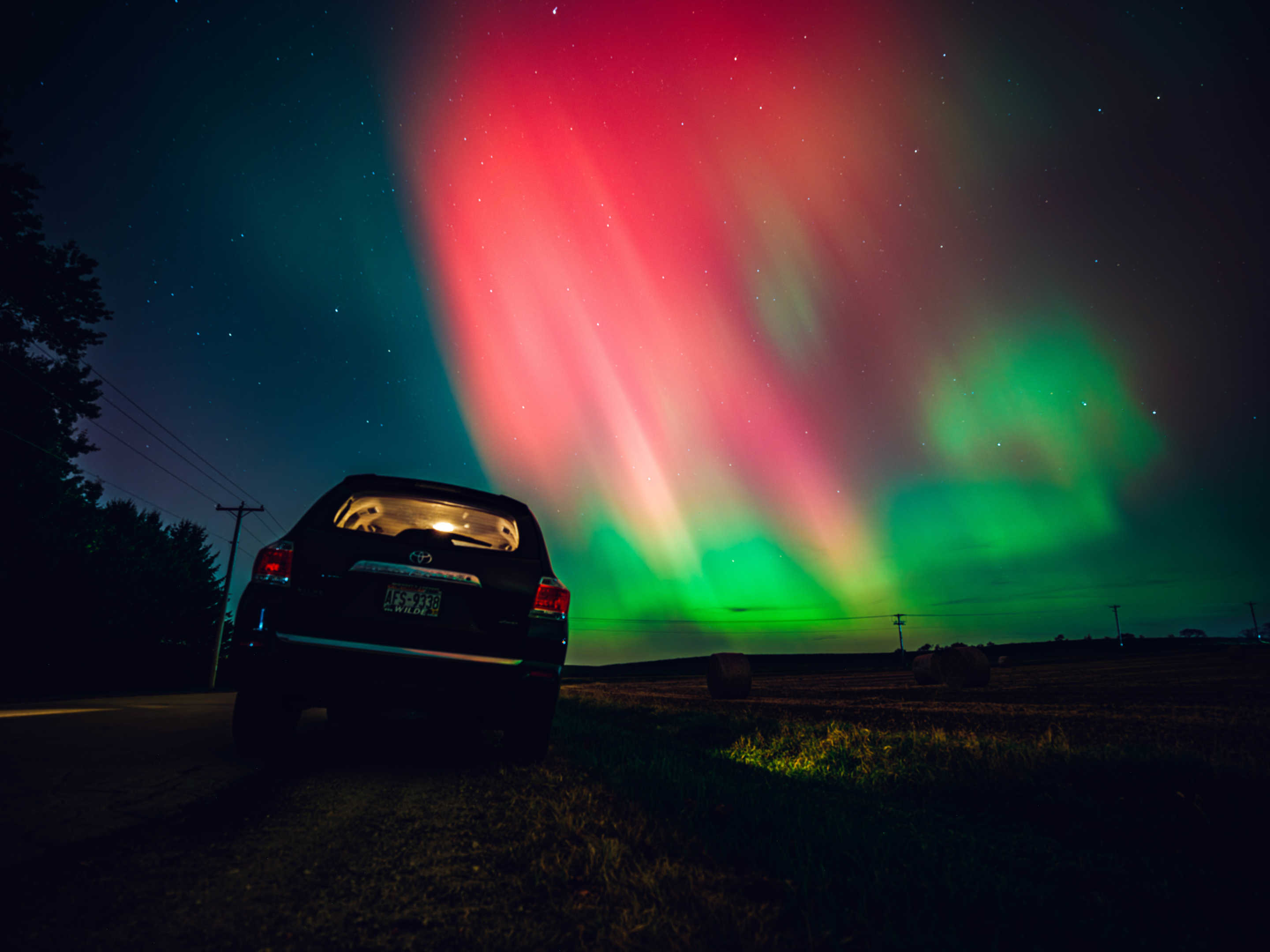 Aurora borealis against the silhouette of a car.