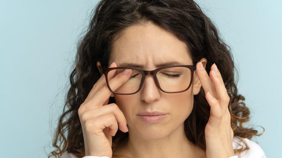 Una mujer con lentes se frota los ojos.