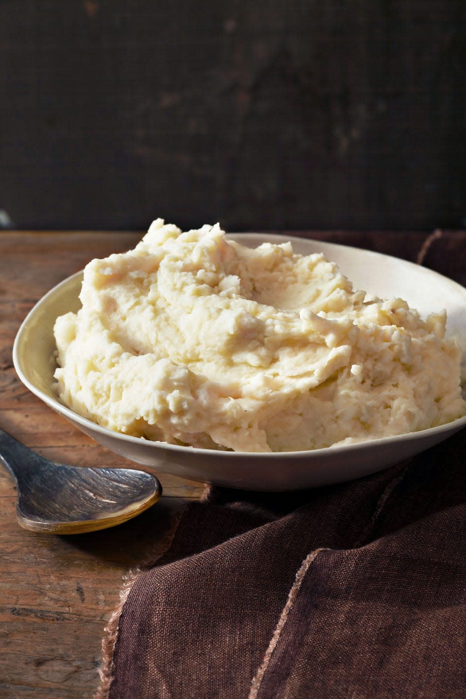 a serving bowl of creamy mashed potatoes with a wooden spoon next to it