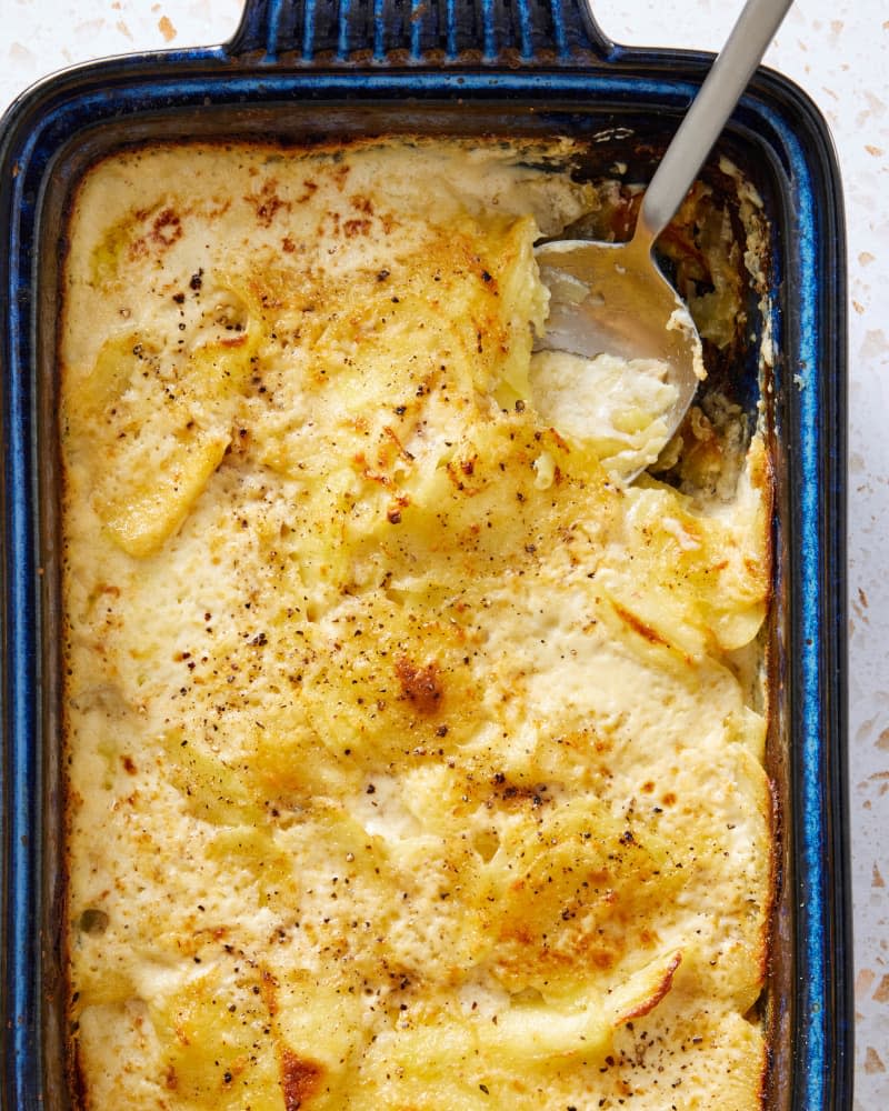 A blue baking dish full of Cacio e Pepe Potato Gratin with a serving spoon inserted.