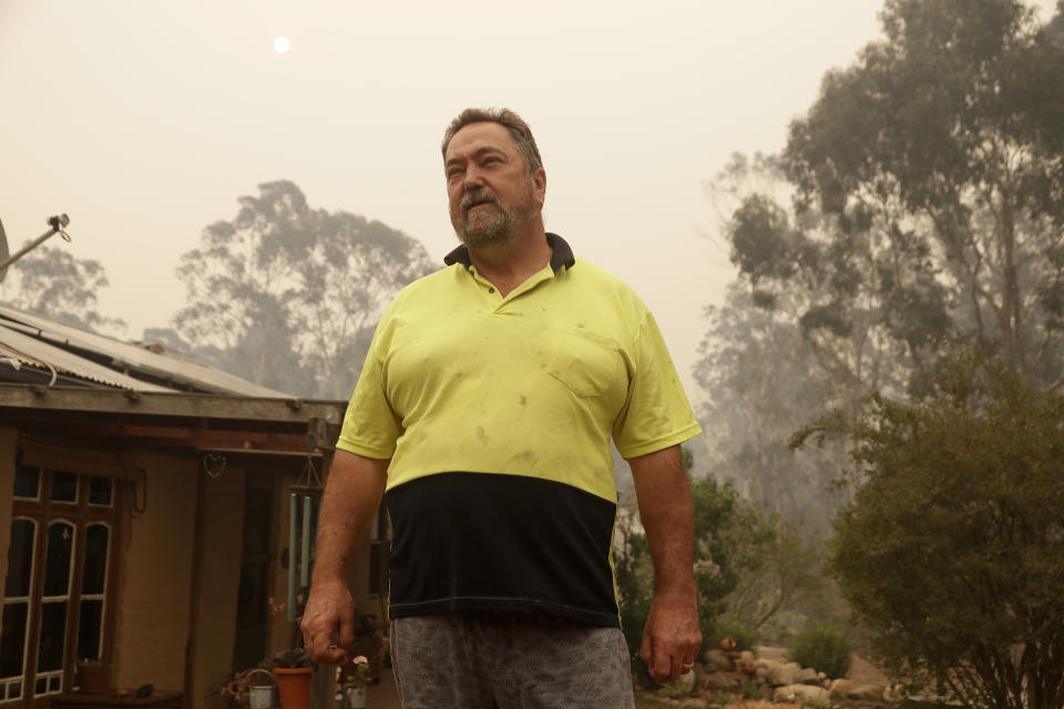 In this Jan, 11, 2020, photo, Joe Seamons stands outside his house at Burragate, Australiaa day after an anticipated wildfire impact failed to come. It seemed imminent to those hunkering at the fire station that "The Beast" would finally roar through. But on this night the wildfire only crept closer, prodding forward a few tentative fingers before going dormant again as the winds died. (AP Photo/Rick Rycroft)