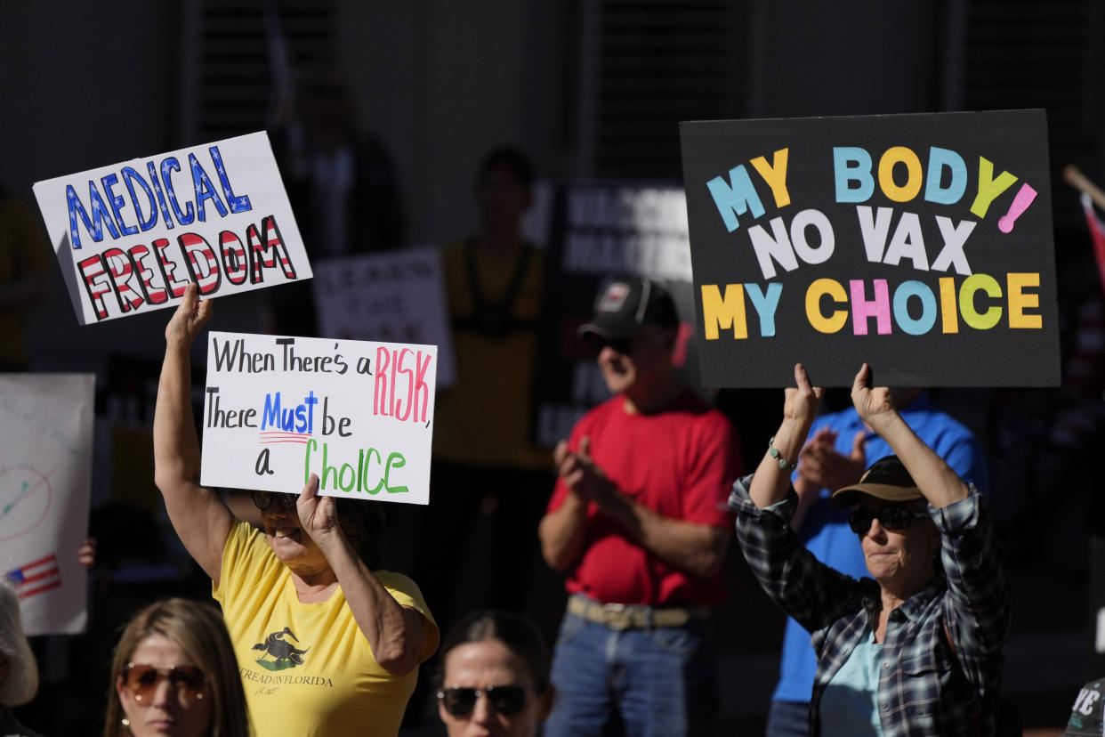 FILE - People hold signs as several hundred anti-mandate demonstrators rally outside the Capitol during a special legislative session considering bills targeting COVID-19 vaccine mandates, Nov. 16, 2021, in Tallahassee, Fla. The vaccines’ first year has been rocky with the disappointment of breakthrough infections, the political strife over mandates and, now, worries about whether the mutant omicron will evade the vaccine's protection. (AP Photo/Rebecca Blackwell, File)