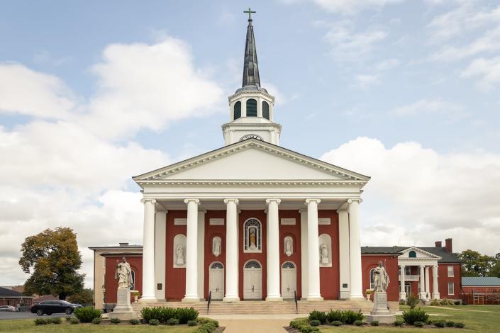 A Catholic Church in Bardstown, Kentucky is made out of red brick with a tall white steeple and pillars