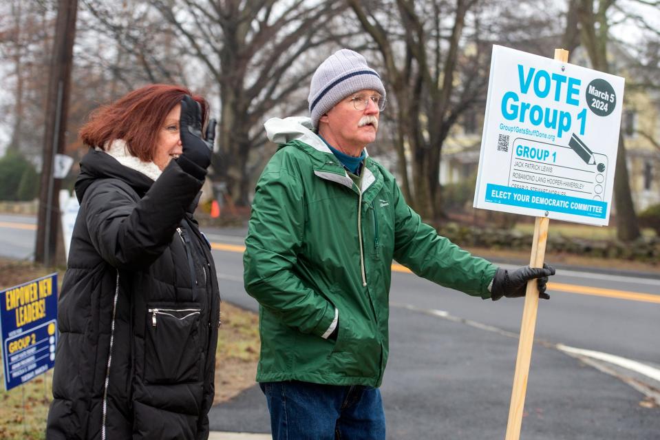 Katie Murphy, left, and Larry Stoodt wave to passing vehicles outside the Brophy Elementary School polling location in Framingham, March 5, 2024. Murphy and Stoodt were each elected to the Framingham Democratic Committee as part of the Group 1 slate.