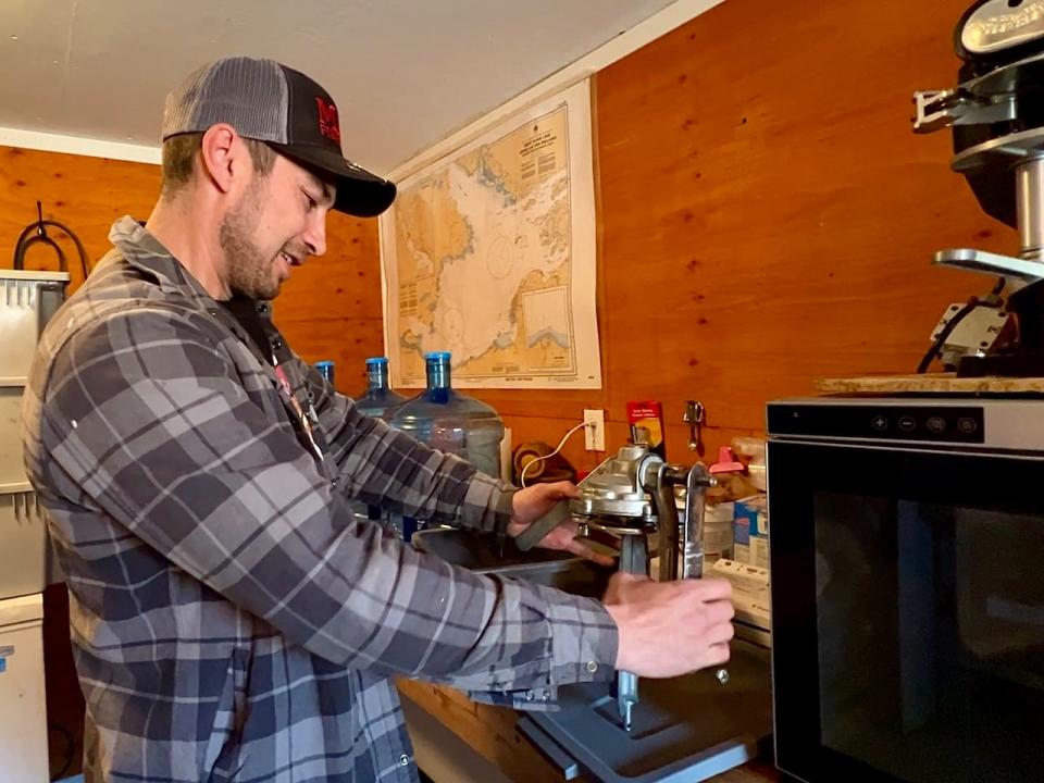 Campbell inside MAG Fisheries & Cannery holding the first manual can sealer they used to can fish, he estimates it sealed 1300 cans. They have now moved to an automated can sealer.