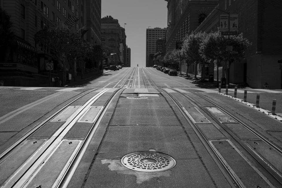 Empty cable car tracks lead up to Nob Hill as a person crosses California Street between the Mark Hopkins and Fairmont hotels in San Francisco on May 1, 2020. Normally, the months leading into summer bring bustling crowds to the city's famous landmarks, but this year, because of the coronavirus threat they sit empty and quiet. Some parts are like eerie ghost towns or stark scenes from a science fiction movie. (AP Photo/Eric Risberg)