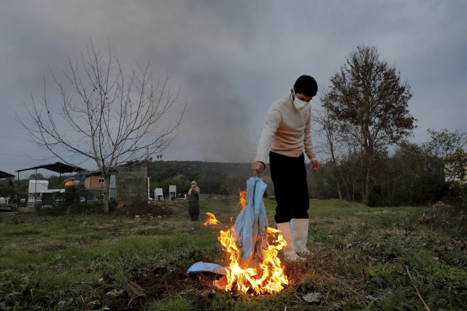 Mohammad Hossein Khoshnazar, 18, a cleric volunteer burns his protective clothes after the funeral of Ghorbanali Mahmoudi, 59, who died from COVID-19 at a cemetery in the Haji Kola village on the outskirts of the city of Ghaemshahr, in northern Iran, Saturday, Dec. 19, 2020. (AP Photo/Ebrahim Noroozi)