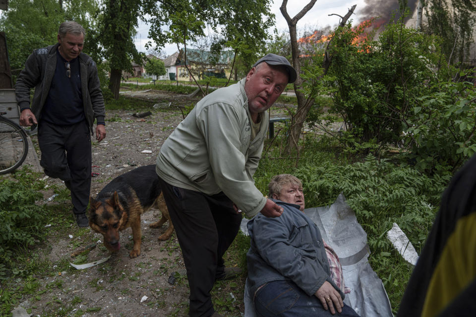 A man gives his neighbour pills as his house is seen on fire after a Russian airstrike in Vovchansk, Ukraine, on Saturday, May 11, 2024. (AP Photo/Evgeniy Maloletka)