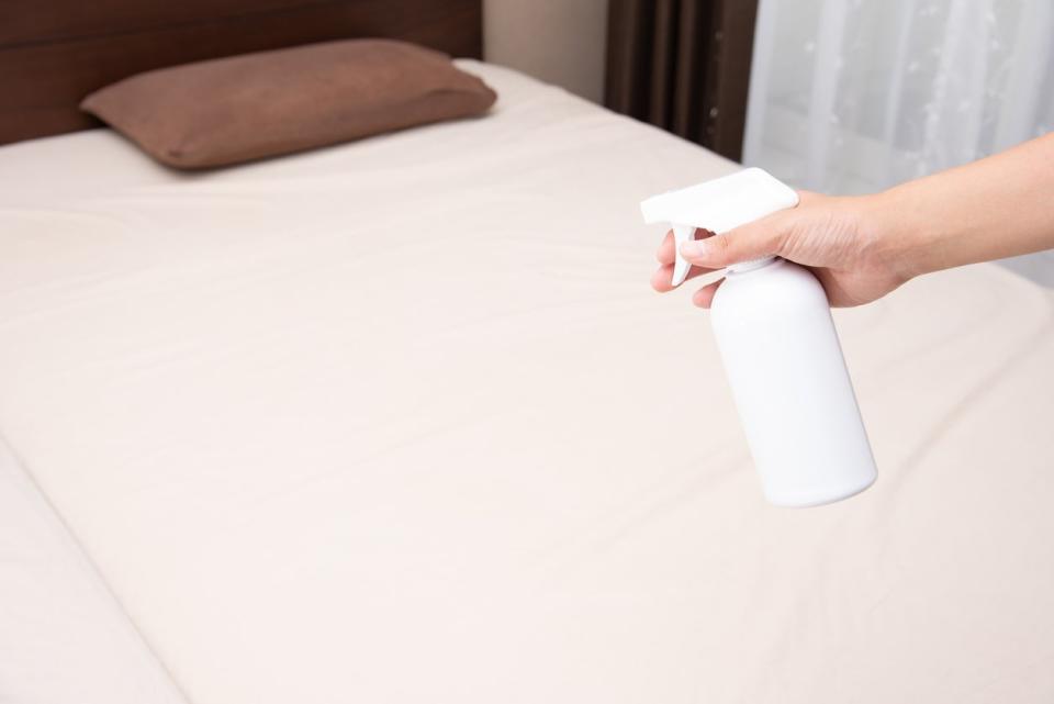 woman spraying a deodorant on a bedroom bed