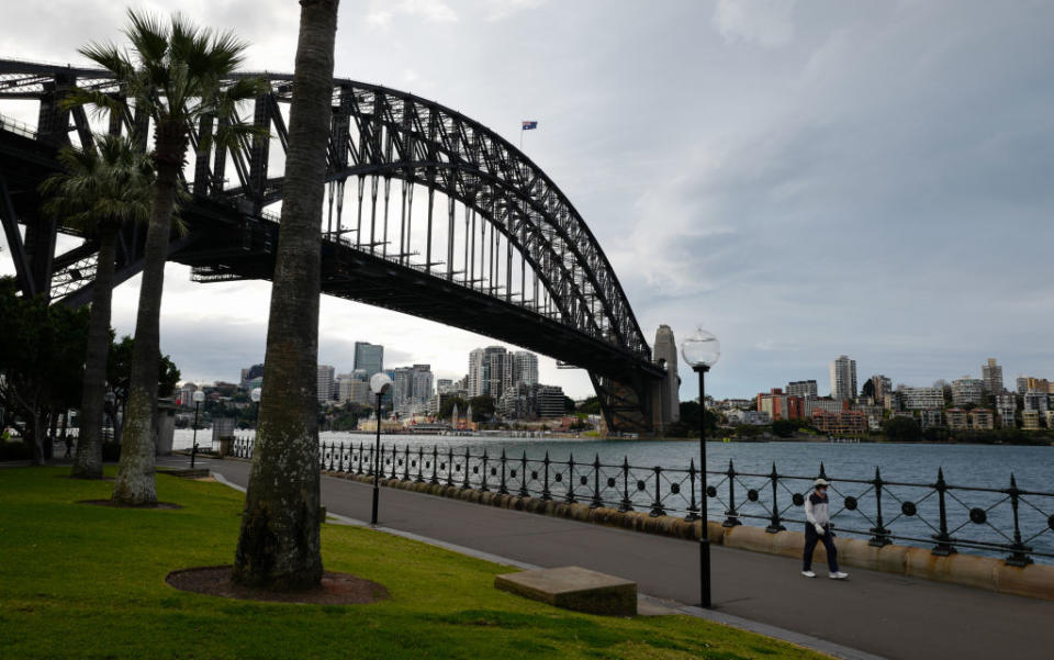 A man wearing a face mask walks beside the Harbour Bridge in Sydney, Australia.