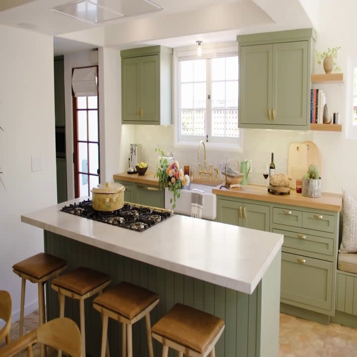 The kitchen has a lot of natural lighting and it has green colored cabinets and the overall look is very clean and sleek