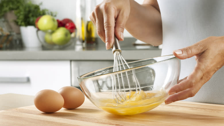 woman whisking eggs in clear bowl