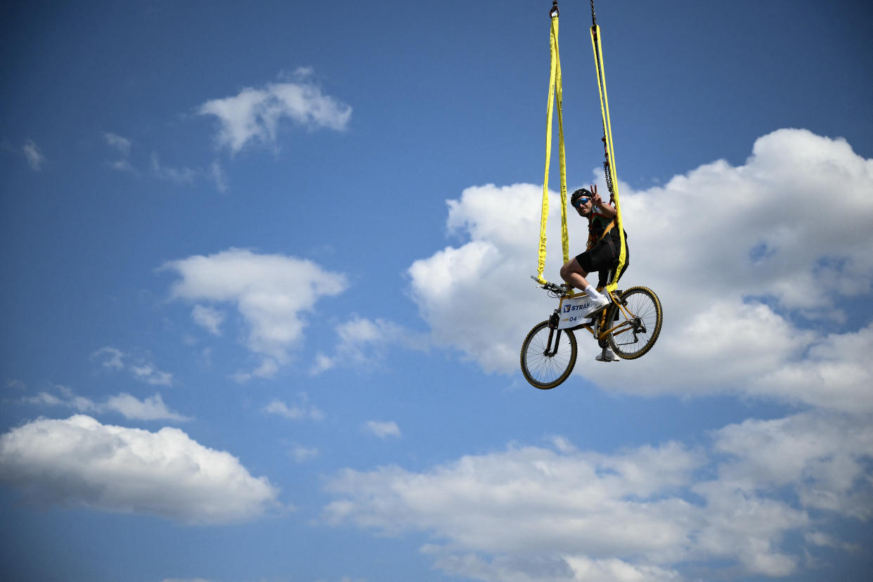 A spectator sits on a bicycle suspended above the race. (Marco Bertorello/AFP via Getty Images)