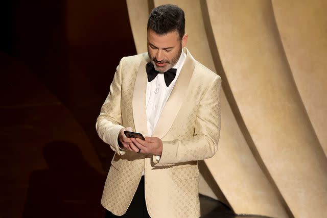 <p>Kevin Winter/Getty</p> Jimmy Kimmel reading Donald Trump's post from his phone on stage at the 2024 Oscars