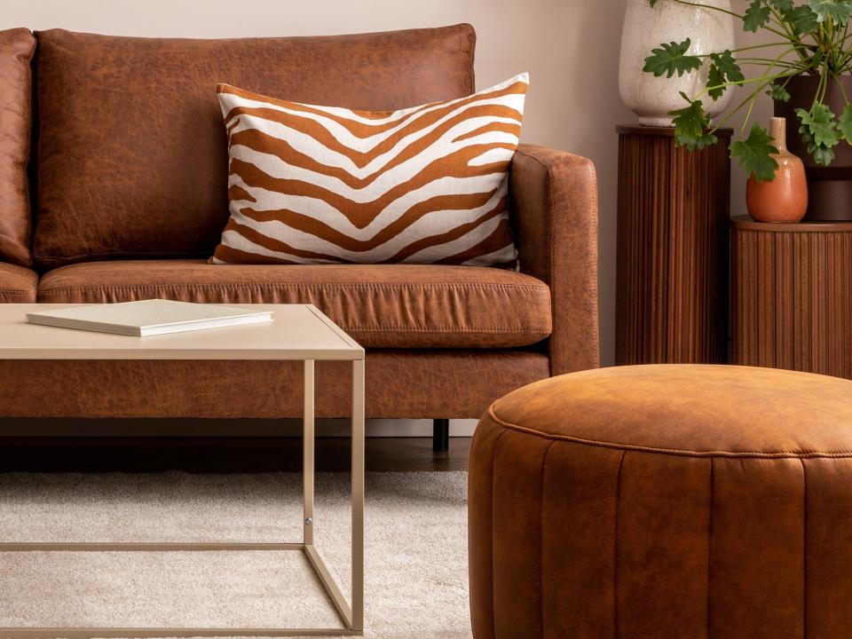 A brown couch next a brown ottoman and a coffee table