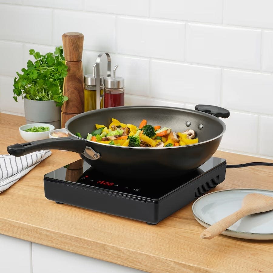 A wok full of veggies sits atop a glossy black rectangular surface on a kitchen counter