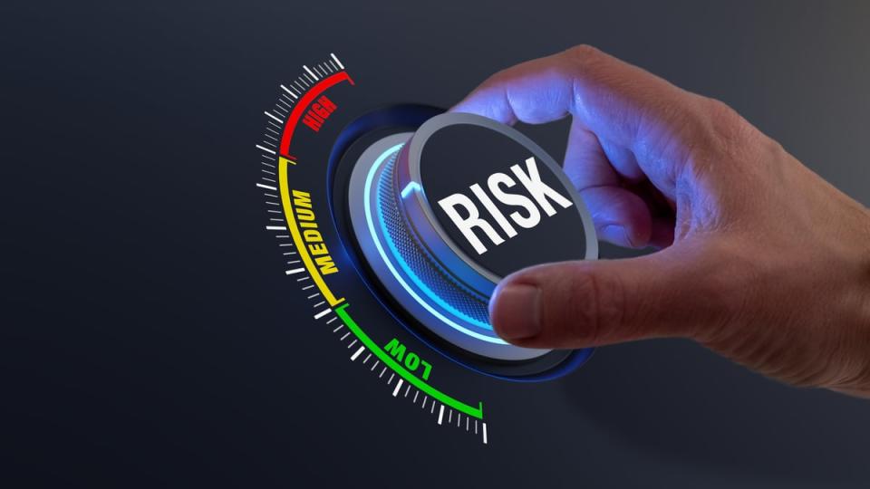 A hand turning up a dial with the word risk on it.