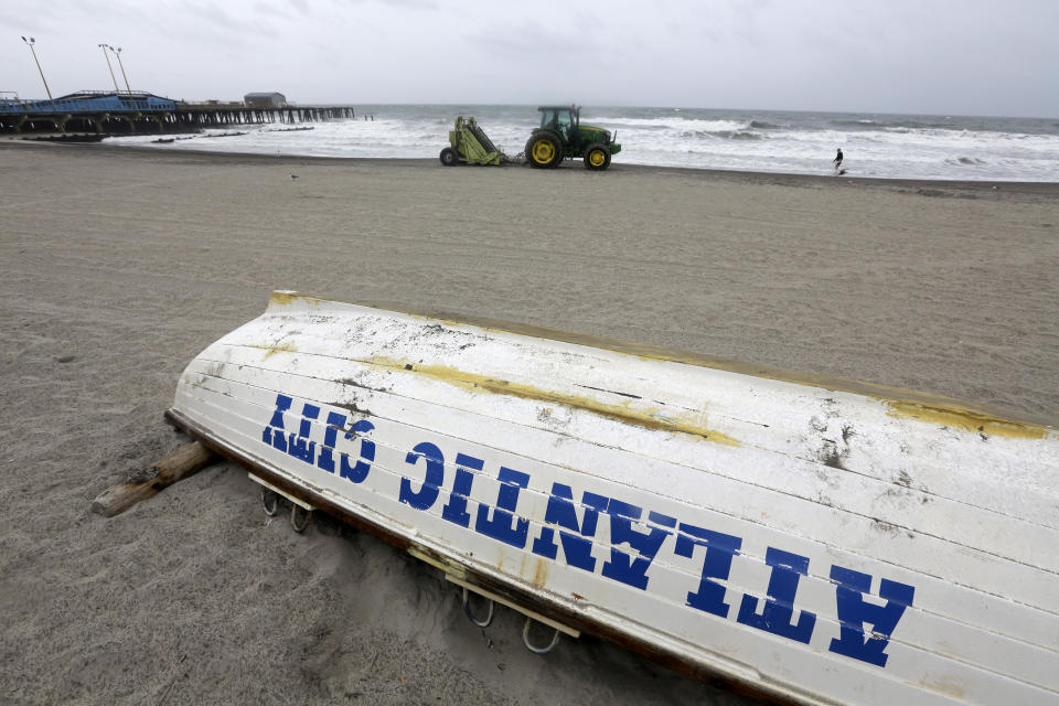 A person walks along the shoreline as a earthmover prepares sand along the beach Tuesday, Aug. 4, 2020, in Atlantic City, N.J. Tropical Storm Isaias spawned tornadoes and dumped rain during an inland march up the U.S. East Coast, including New Jersey, on Tuesday after making landfall as a hurricane along the North Carolina coast. (AP Photo/Jacqueline Larma)