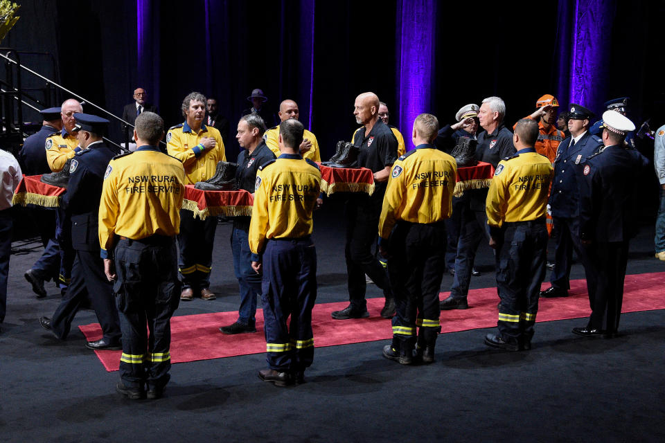 Fire boots representing the six RFS and Coulson Aviation firefighters killed in the recent bush fires are carried through a guard of honour at the Bushfire State Memorial at Qudos Bank Arena in Sydney, Sunday, February 23, 2020. (AAP Image/Bianca De Marchi) NO ARCHIVING