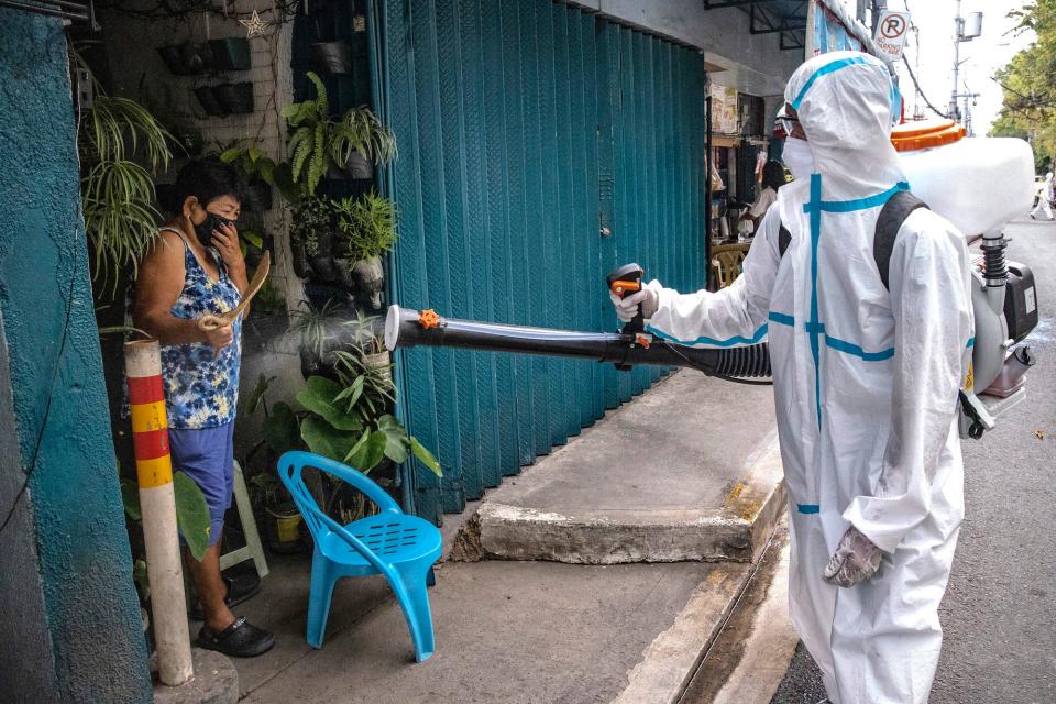 A woman reacts as a disinfection worker sprays disinfectant along a street at a suburban area on March 23, 2020 in San Juan, Metro Manila, Philippines.