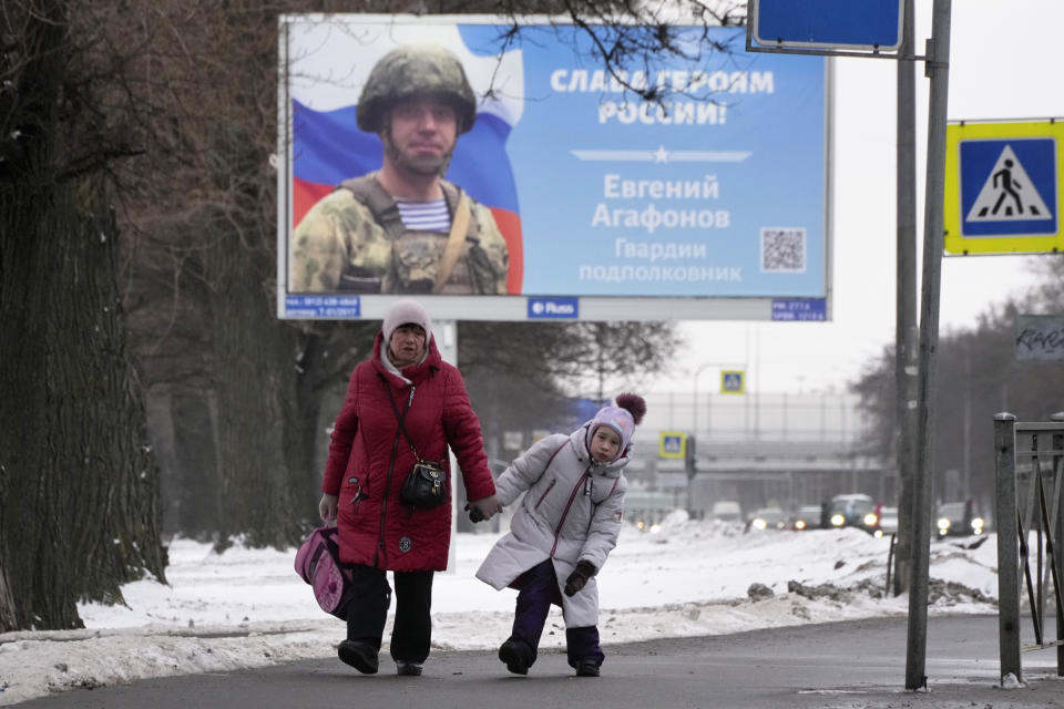 A woman and a girl walk past a billboard with a portrait of a Russian officer awarded for action in Ukraine and the words "Glory to the heroes of Russia" in St. Petersburg, Russia, Wednesday, Jan. 11, 2023. (AP Photo/Dmitri Lovetsky)