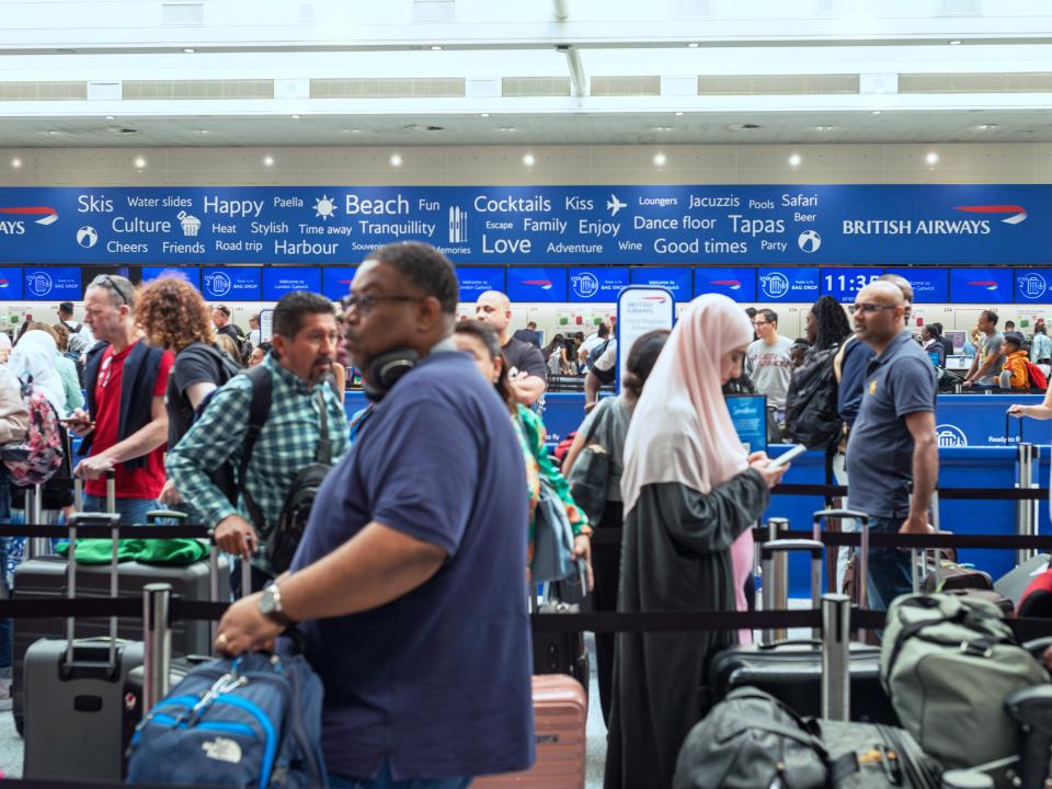 People queue to check in for flights at Gatwick Airport with a blue sign in the background.