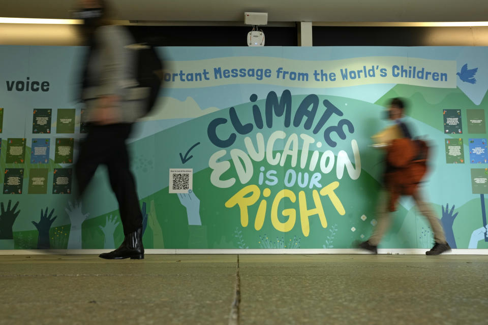 People walk past a wall with a message on climate eduction at the COP26 U.N. Climate Summit in Glasgow, Scotland, Sunday, Oct. 31, 2021. The U.N. climate summit in Glasgow formally opens Sunday, a day before leaders from around the world gather in Scotland's biggest city to lay out their vision for addressing the common challenge of global warming. (AP Photo/Alastair Grant)