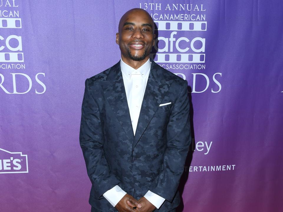 charlemagne tha god wearing a navy suit in front of a purple background at the 13th annual african american film critics film honors in los angeles