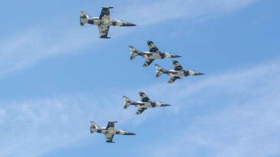 Fünf Jets fliegen in Formation am blauen Himmel.