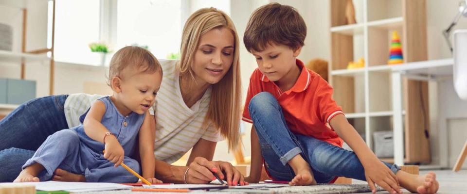 Young mother and little children drawing picture together sitting on floor.