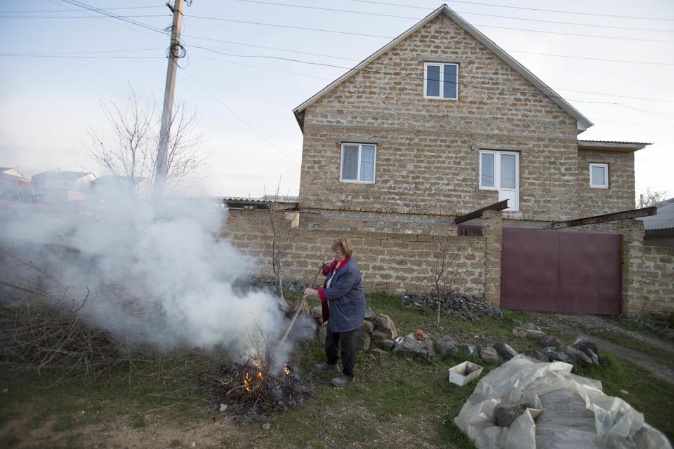 In this photo taken Thursday March 27, 2014 Crimea's Tatar Setyaya Murtazayev's wife, Russian Galina, 56, burns leaves outside of their long-standing squatter settlement, in Pionerskoye not far from Simferopol, Crimea. On Saturday the Crimean Tatar Qurultay, a religious congress will determine whether the Tatars will accept Russian citizenship and the political system that comes with it, or remain Ukrainian citizens on Russian soil. (AP Photo/Pavel Golovkin)