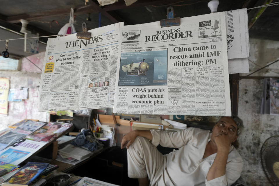 FILE - A vendor sits beside a copy of a morning newspaper which reports missing Titanic submersible and onboard five people, including Pakistani nationals Shahzada Dawood and his son Suleman, at a stall, in Karachi, Pakistan on June 21, 2023. The saga of a lost submersible that had gone into the depths of the ocean to see the Titanic wreckage rippled across the national and global conversation. But a far bigger disaster days earlier, the wrecking of a ship off Greece filled with migrants, didn't become a moment-by-moment worldwide focus in anywhere near the same way. (AP Photo/Fareed Khan, File)