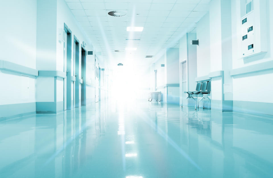 Brightly lit hospital corridor with reflective floor and chairs along the wall