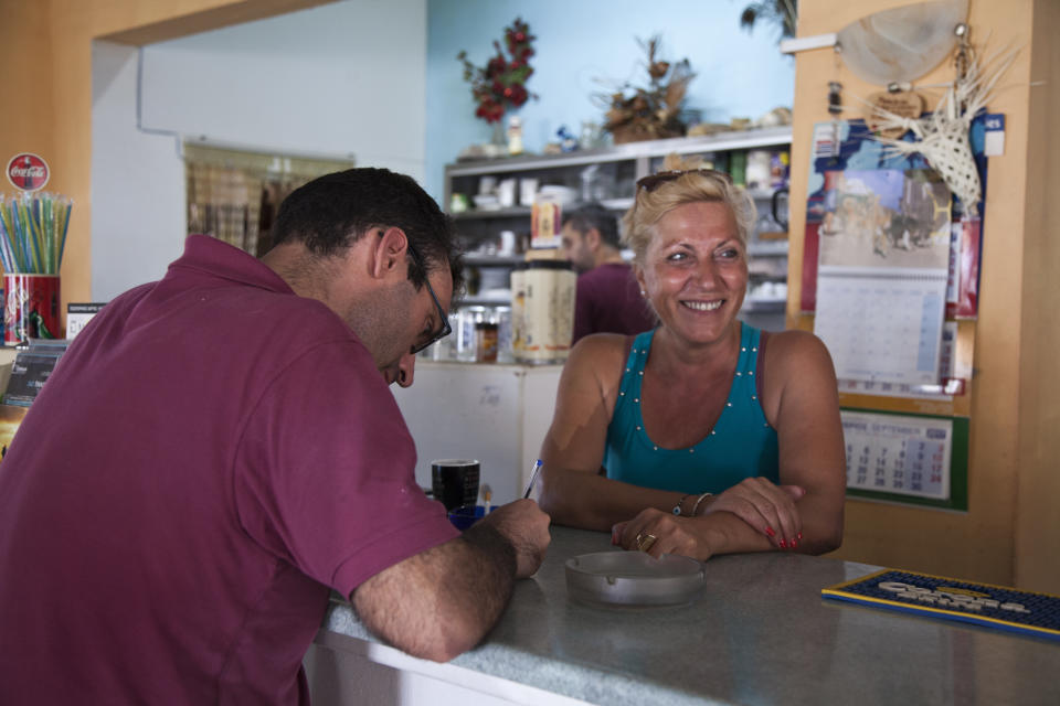 In this Thursday, Aug. 9, 2018, photo people drink coffee in a coffee shop on the Aegean island of Tilos, Greece. Tilos with its winter population of 400 and summer population of some 3000, will become the first island in the Mediterranean to run exclusively on wind and solar power, when the blades of the 800 kilowatt wind turbine start turning. (AP Photo/ Iliana Mier)