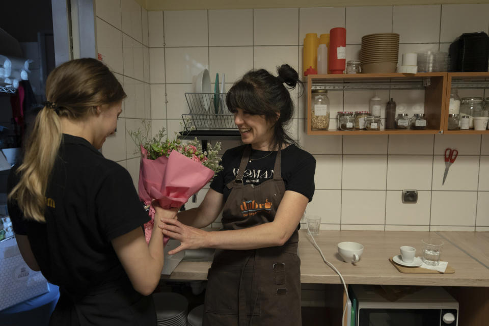 Tetiana Bilous, a Ukrainian refugee from Vinnytsia, right, gives birthday flowers to a colleague in the back room of a coffee shop where she works in the kitchen in Warsaw, Poland, Wednesday, Aug. 17, 2022. (AP Photo/Michal Dyjuk)