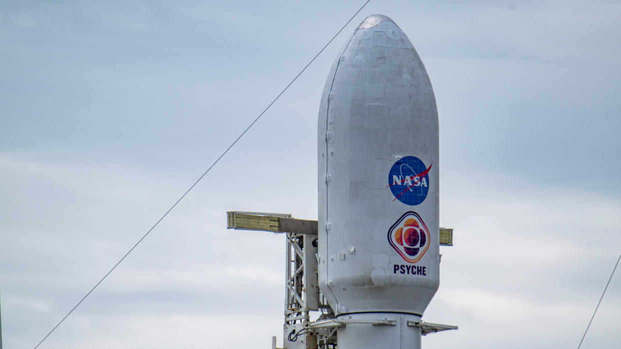 The payload fairings at the top of a rocket stand with cloudy skies behind. 