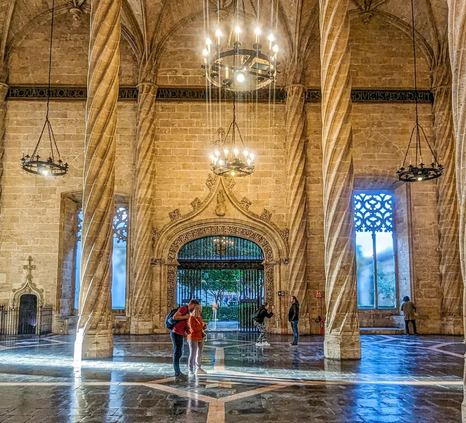 The soaring interior of the Silk Exchange with four slim stone pillars and hanging chandeliers. 