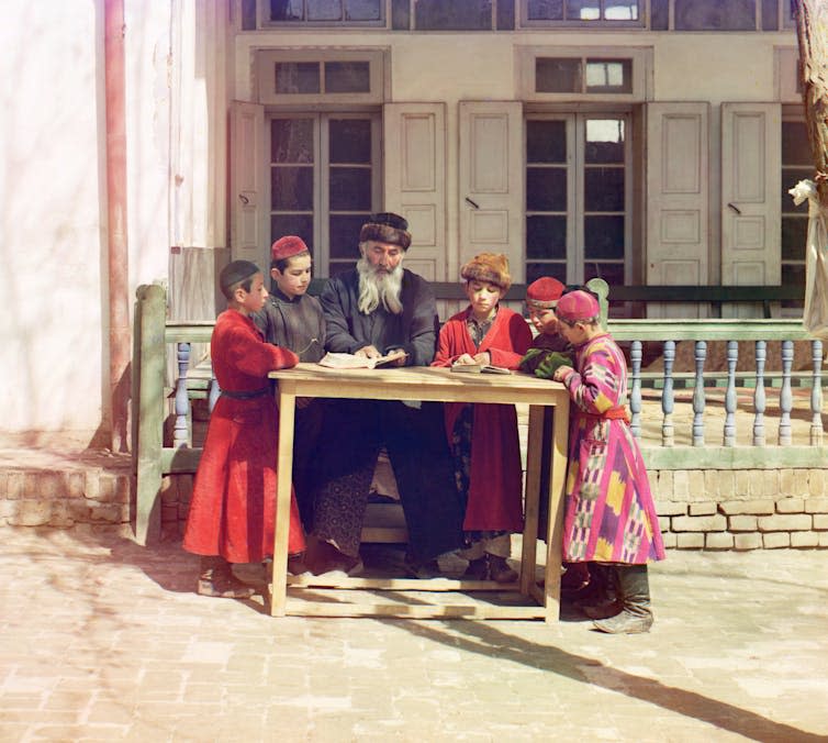 An early colour photograph of a group of children and an old man around a table.